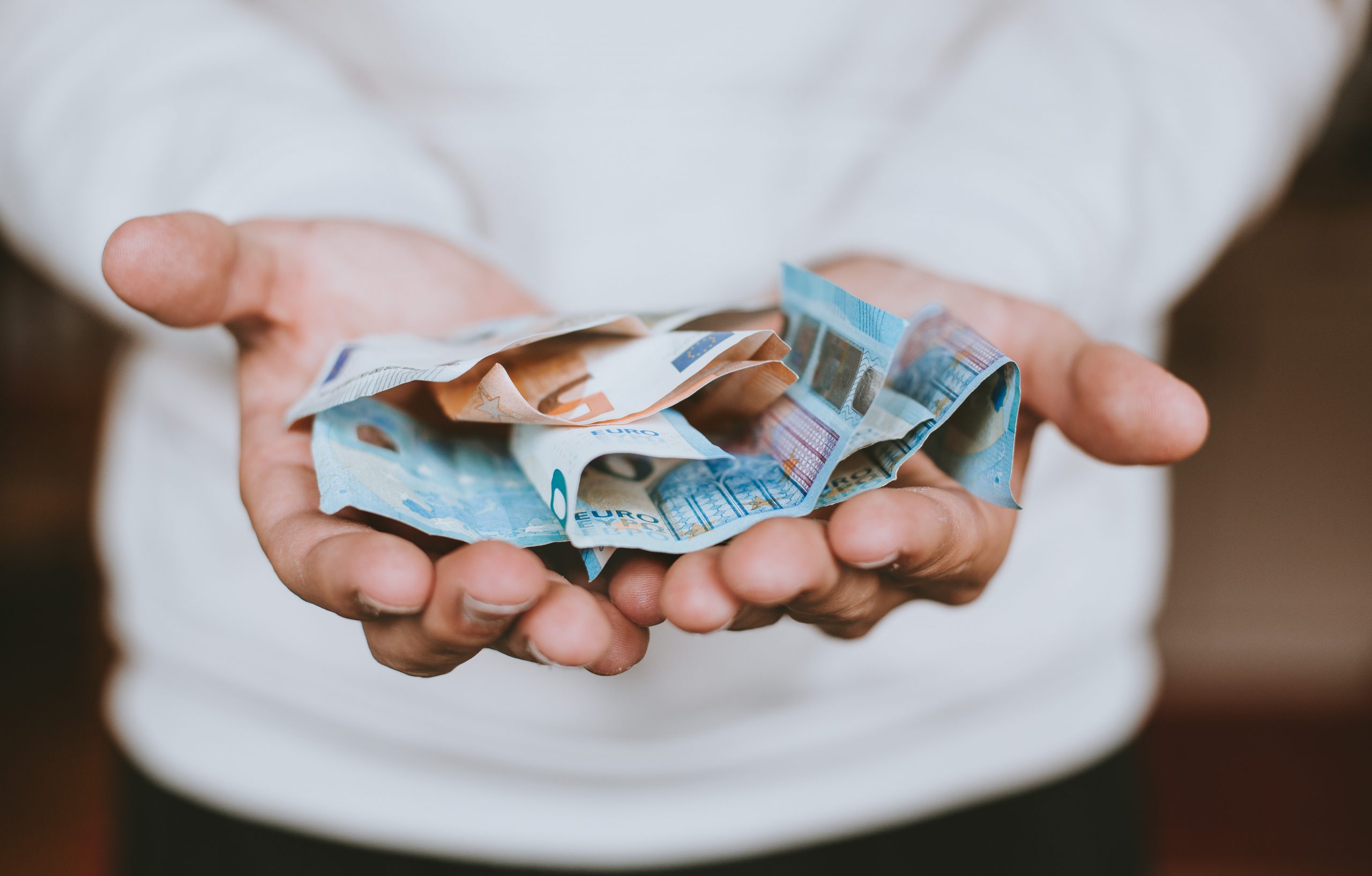 A person with a white shirt holding cash with arms extended