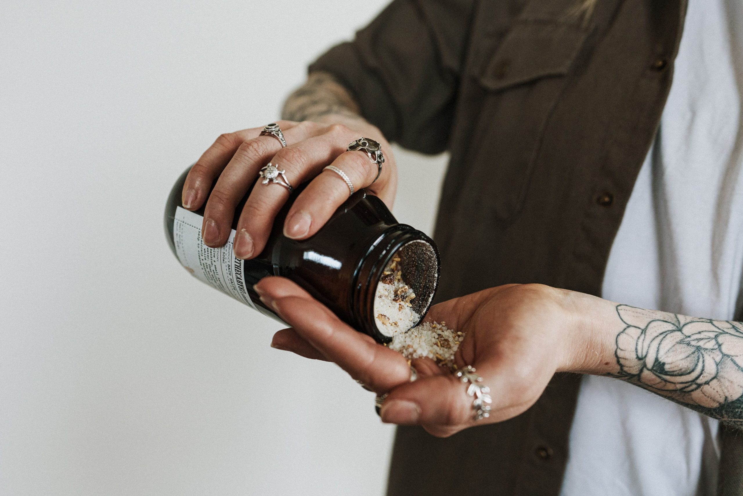 An open bottle of flavored salt being poured by someone onto their left palm set against a white background.