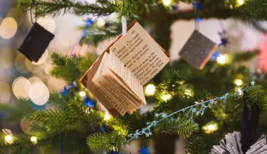 A miniature book decoration hanging from a Christmas tree.