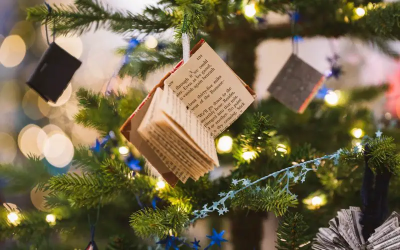 A miniature book decoration hanging from a Christmas tree.