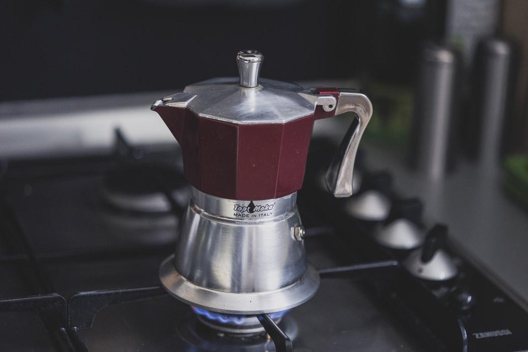 A red colored coffee maker placed on a flaming burner in a kitchen.