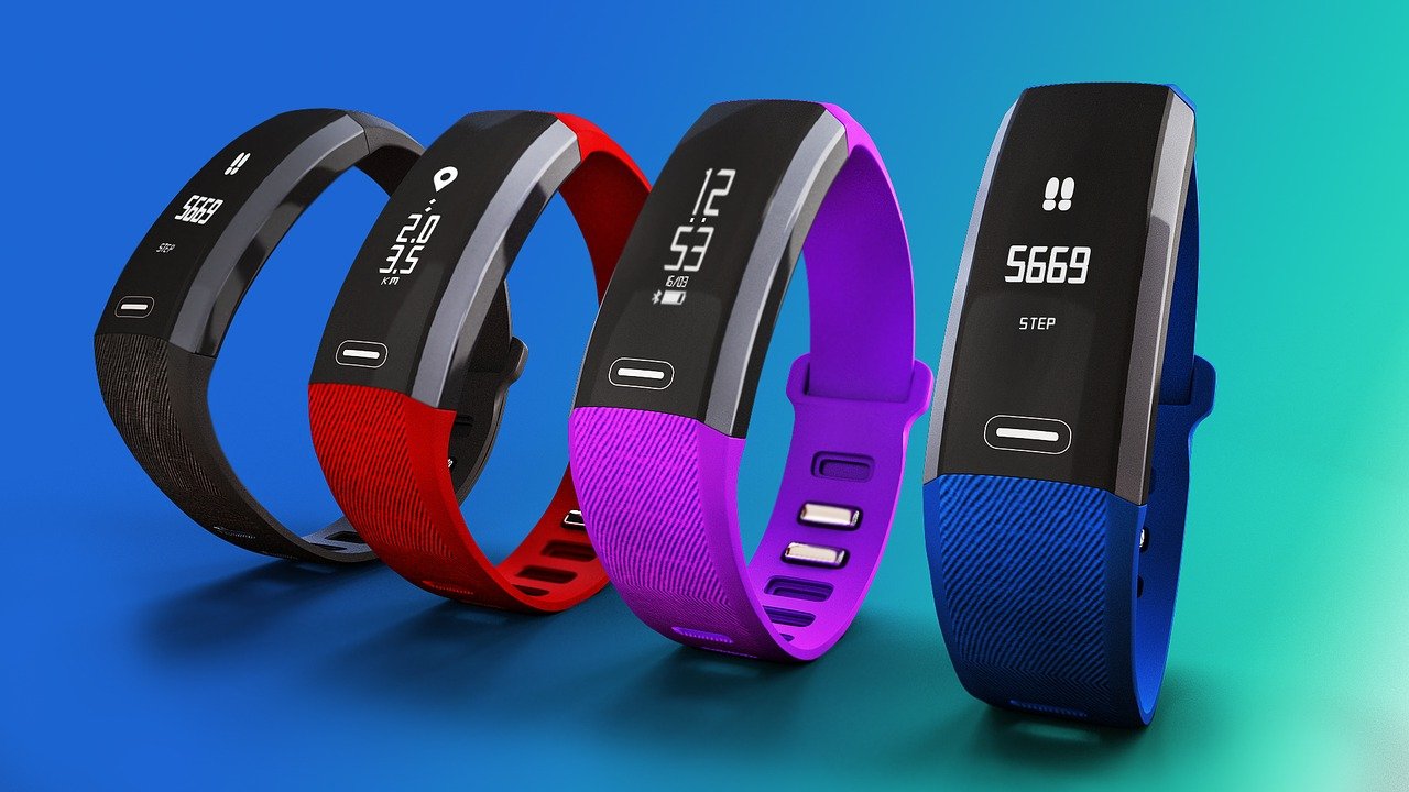 Four fitness trackers in different colors with dials showing the many features