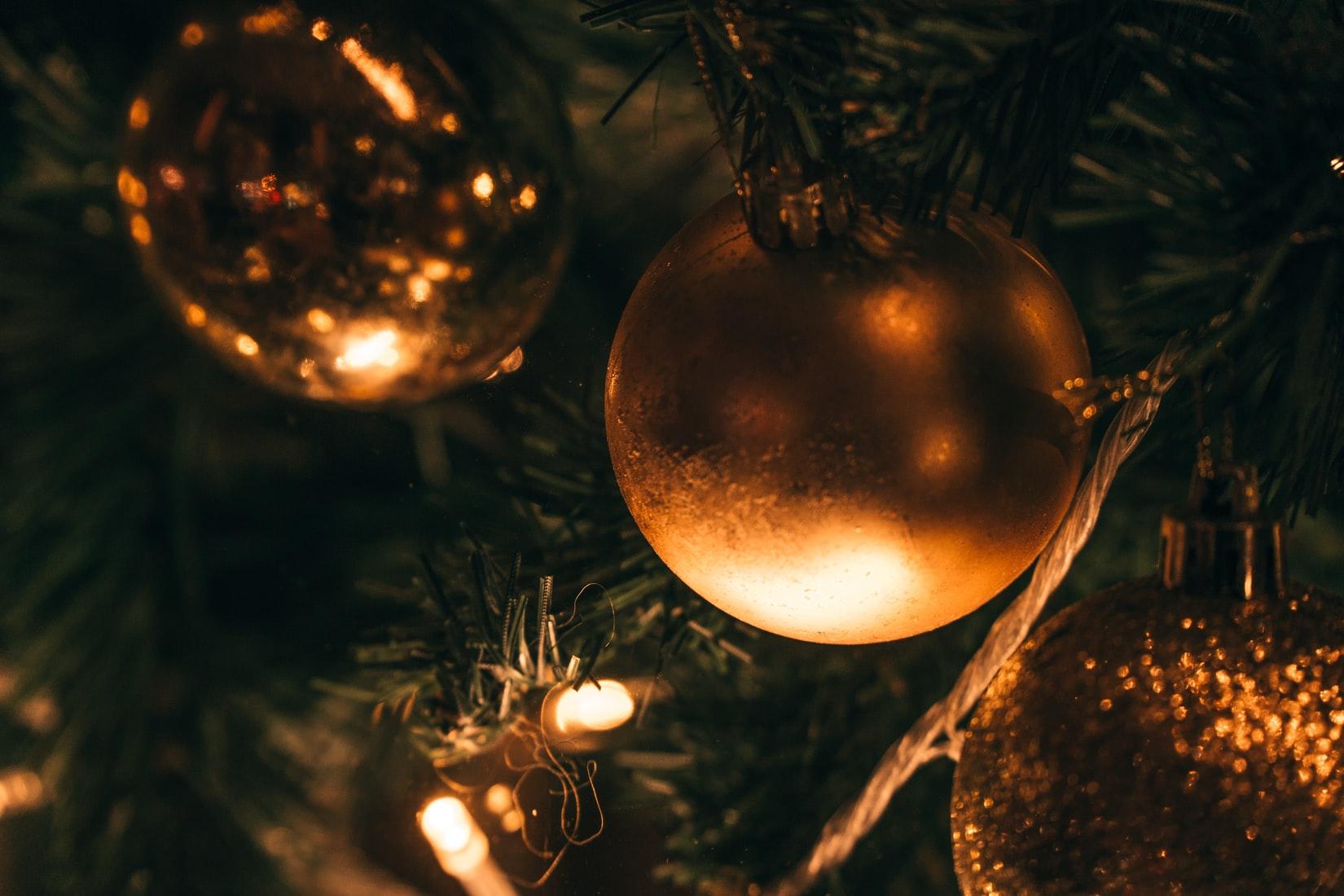 Shiny Christmas baubles hanging from a Christmas tree along with fairy lights.