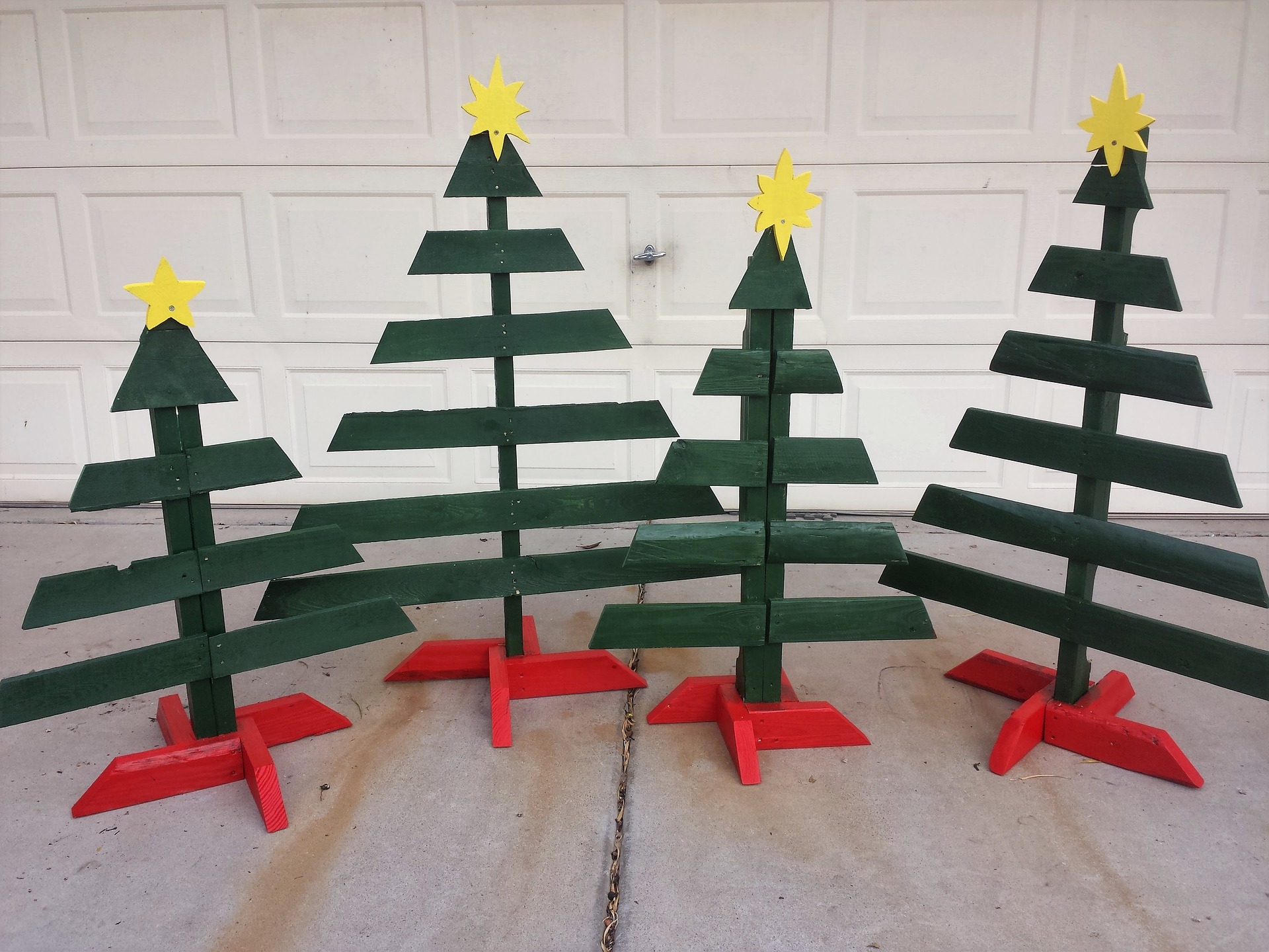 Four handmade Christmas trees of varying sizes featuring wooden boards colored green and red and topped off with yellow stars.