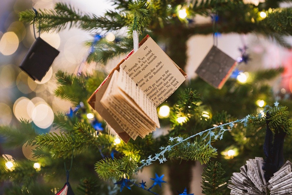A miniature book decoration hanging from a Christmas tree.
