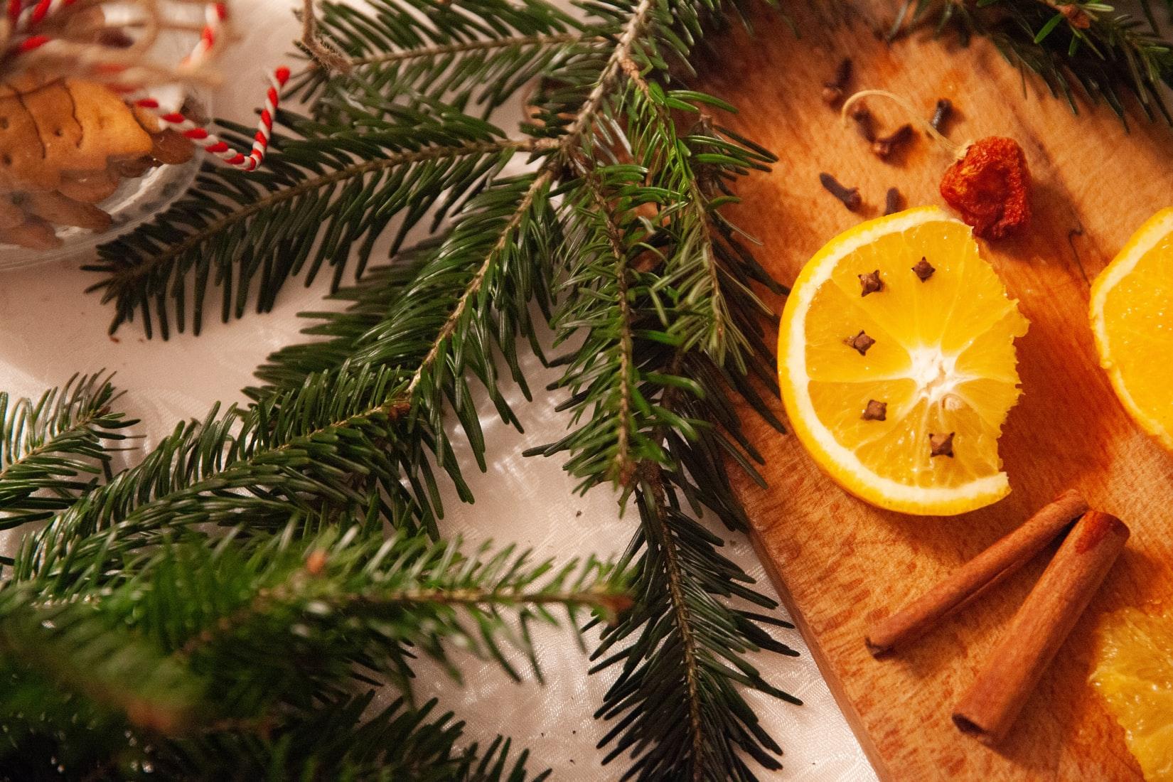 Twigs of rosemary, cinnamon sticks, a slice of citrus fruit and other kitchen spices kept on a surface.