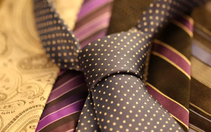 A black shirt tie with yellow polka dots, placed on top of other ties