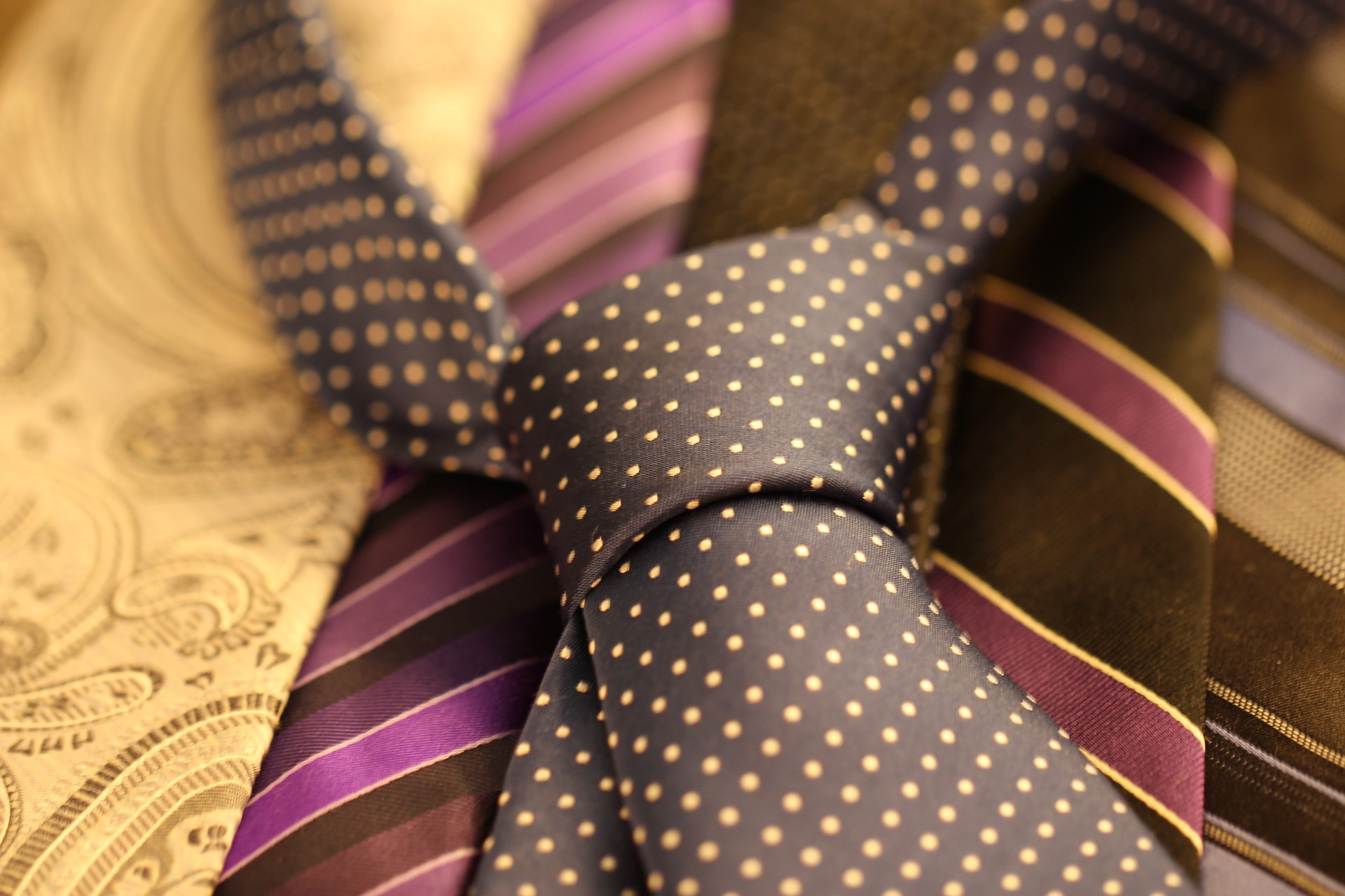 A black shirt tie with yellow polka dots, placed on top of other ties