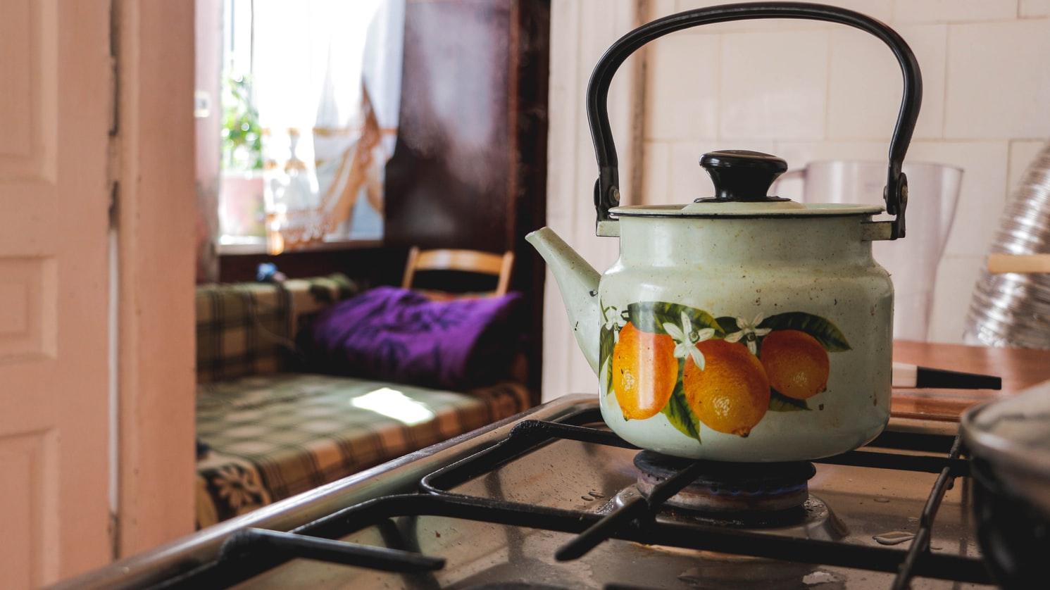 Tea kettle with orange design A green colored tea kettle kept on a closed flame in a kitchen.