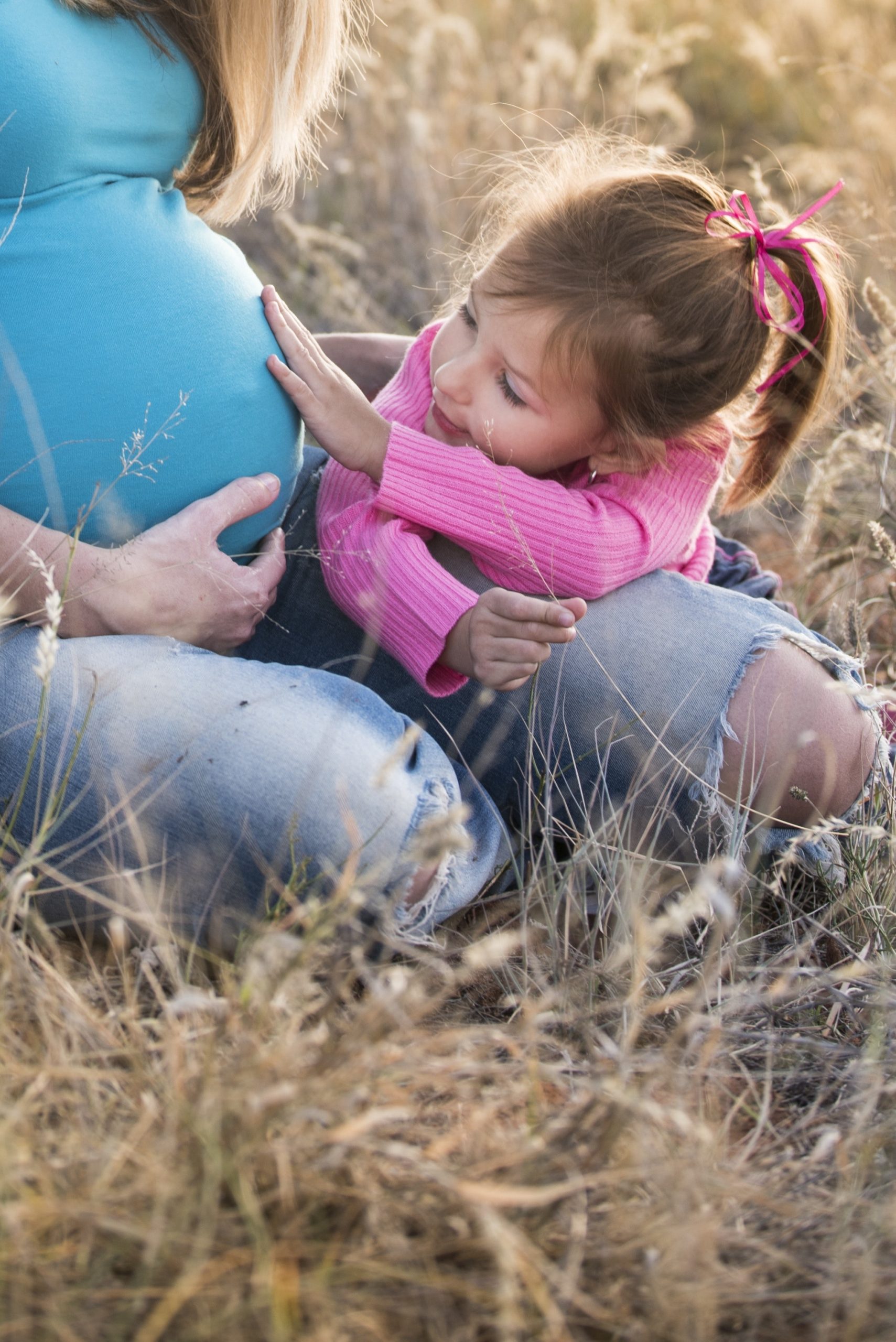 A baby girl dressed in pink touching the belly of a woman dressed in blue