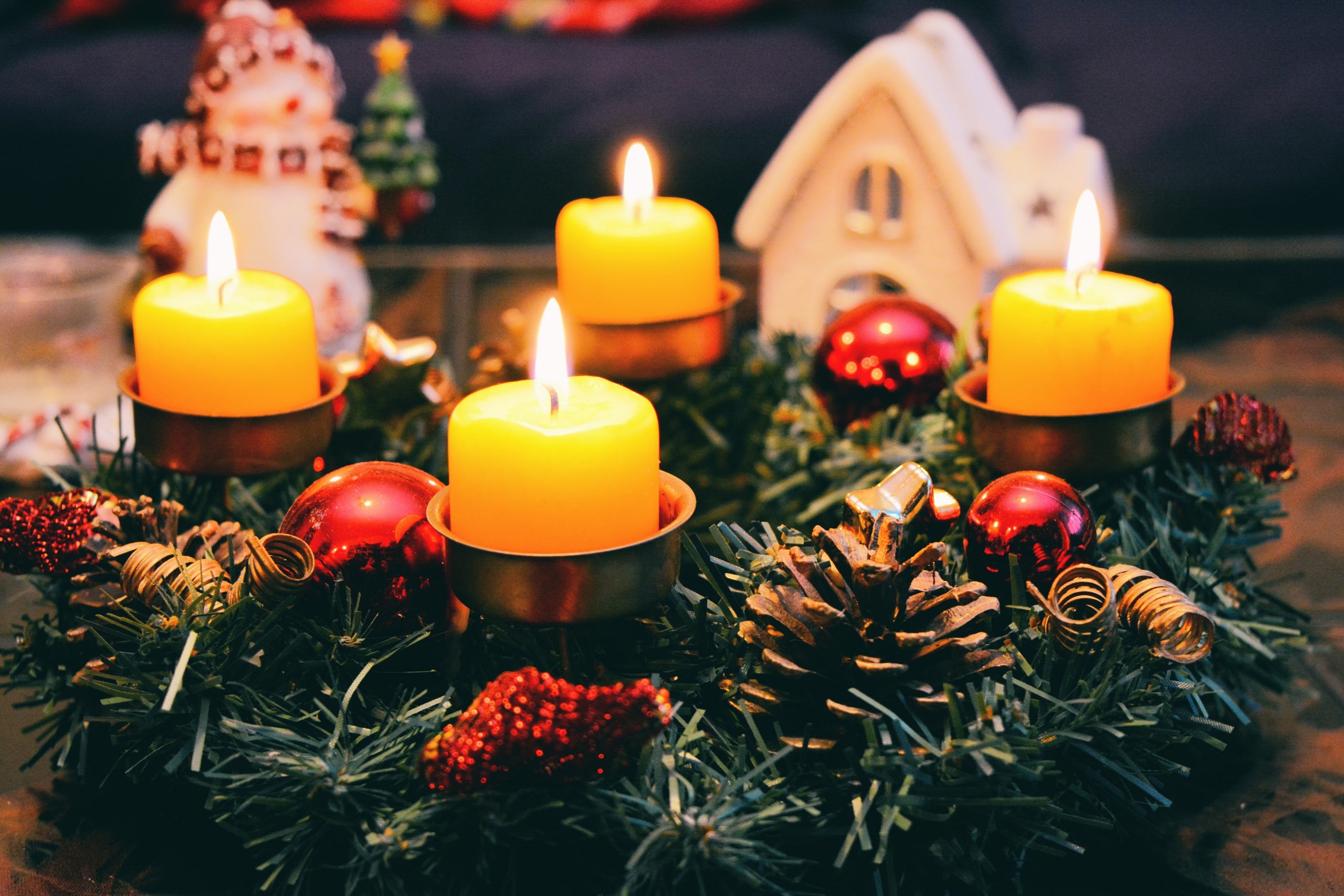 Four yellow candles sitting on top of a Christmas tree decoration featuring pinecones and baubles.