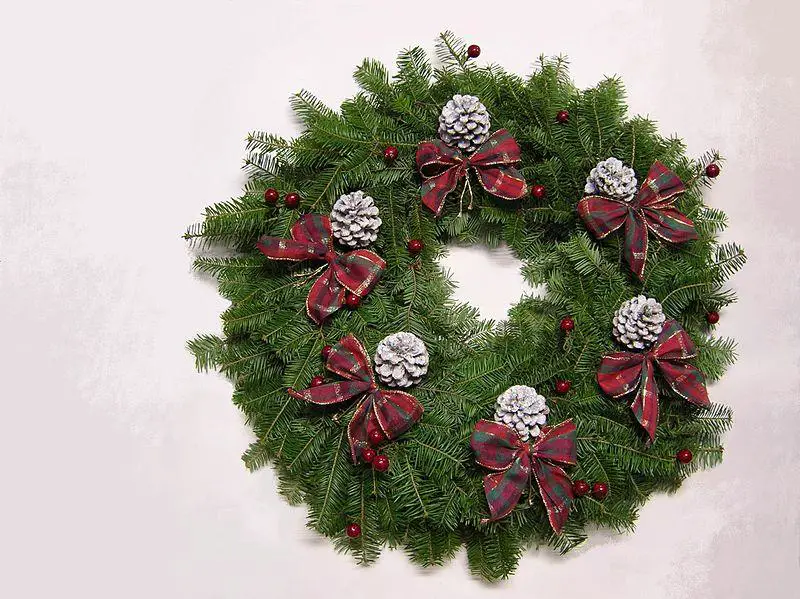 A colorful buffalo plaid Christmas wreath decorated with flowers, cherries, greenery, pine cones, and ribbons. 