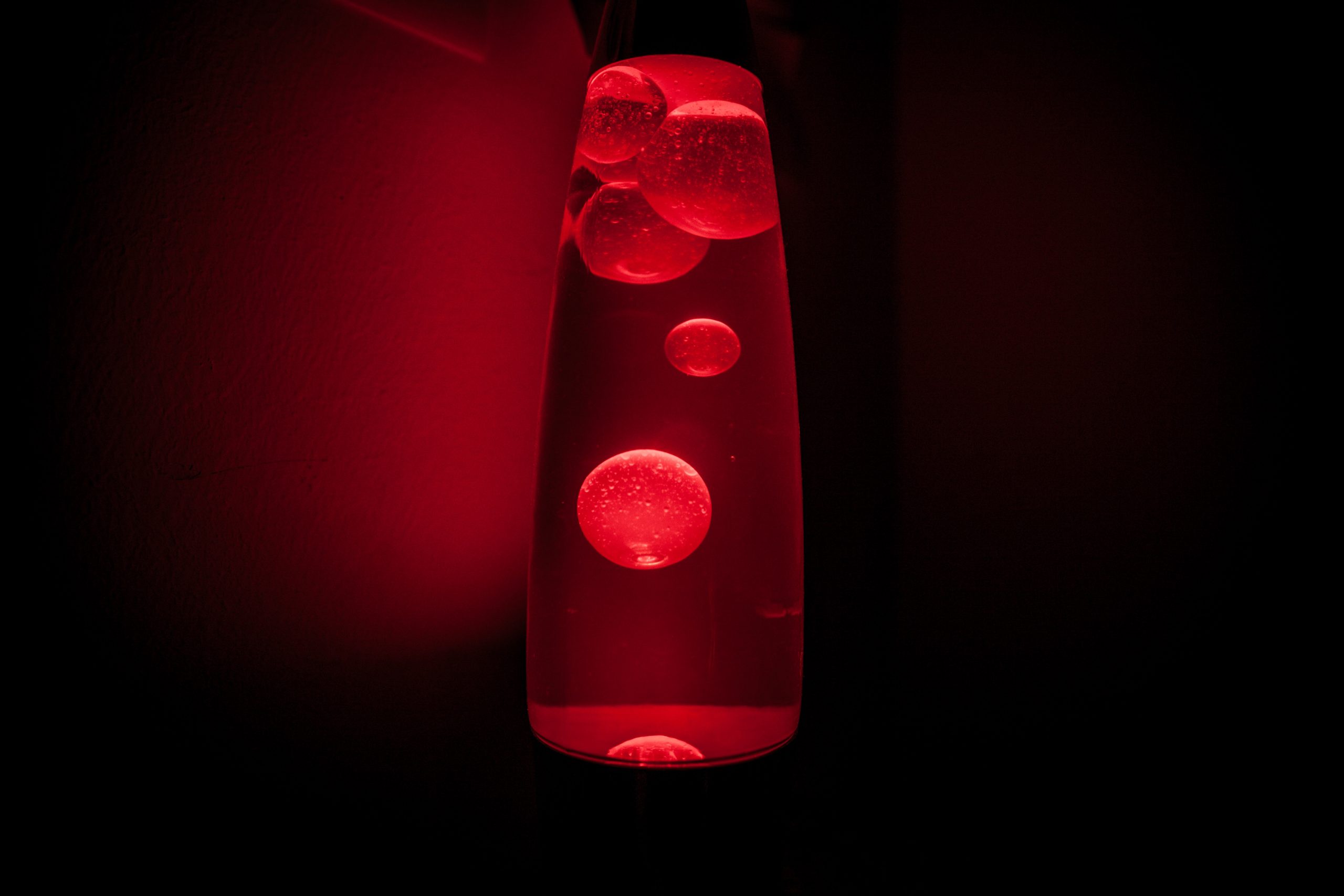 A cylindrical lava lamp emitting red light with its wax floating inside.