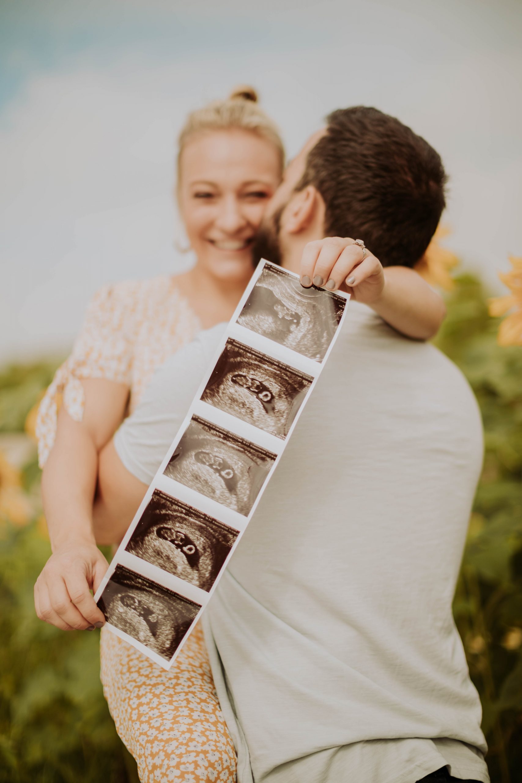 A couple embraced in a loving hug with the woman holding a photo montage of her sonogram