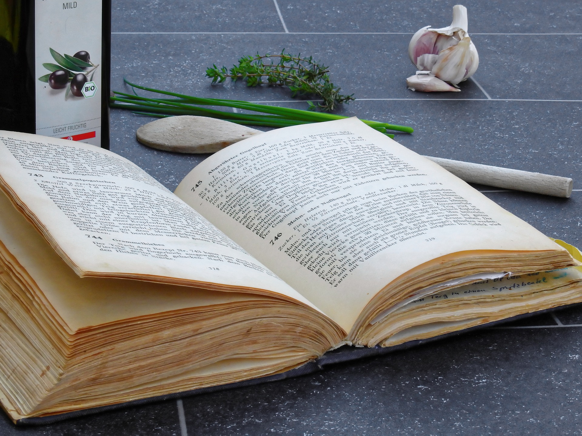 An open cookbook; olive oil bottle and other ingredients nearby.