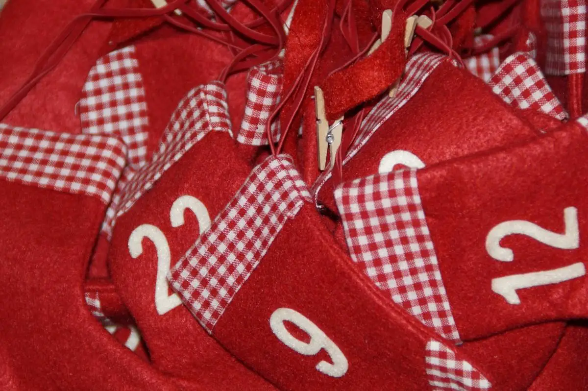 A chair with a buffalo plaid Christmas stocking hanging from it, utensils and Christmas theme shaped cookies, and a stand with a box and Christmas decoration 