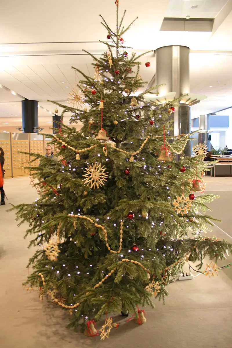 A Christmas tree that is decorated mostly with red balls, golden bells, stars and strings, and white lights.