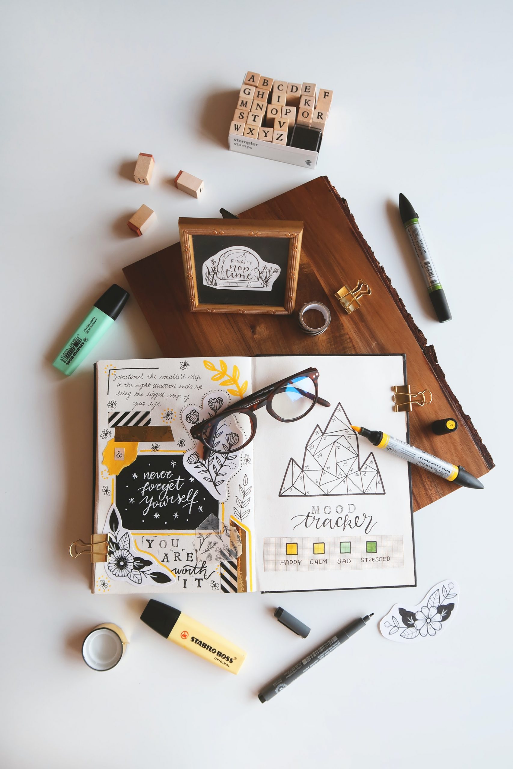 Open journal with a mood tracker A journal with several designs, quotes, and a mood tracker against a brown and white background.