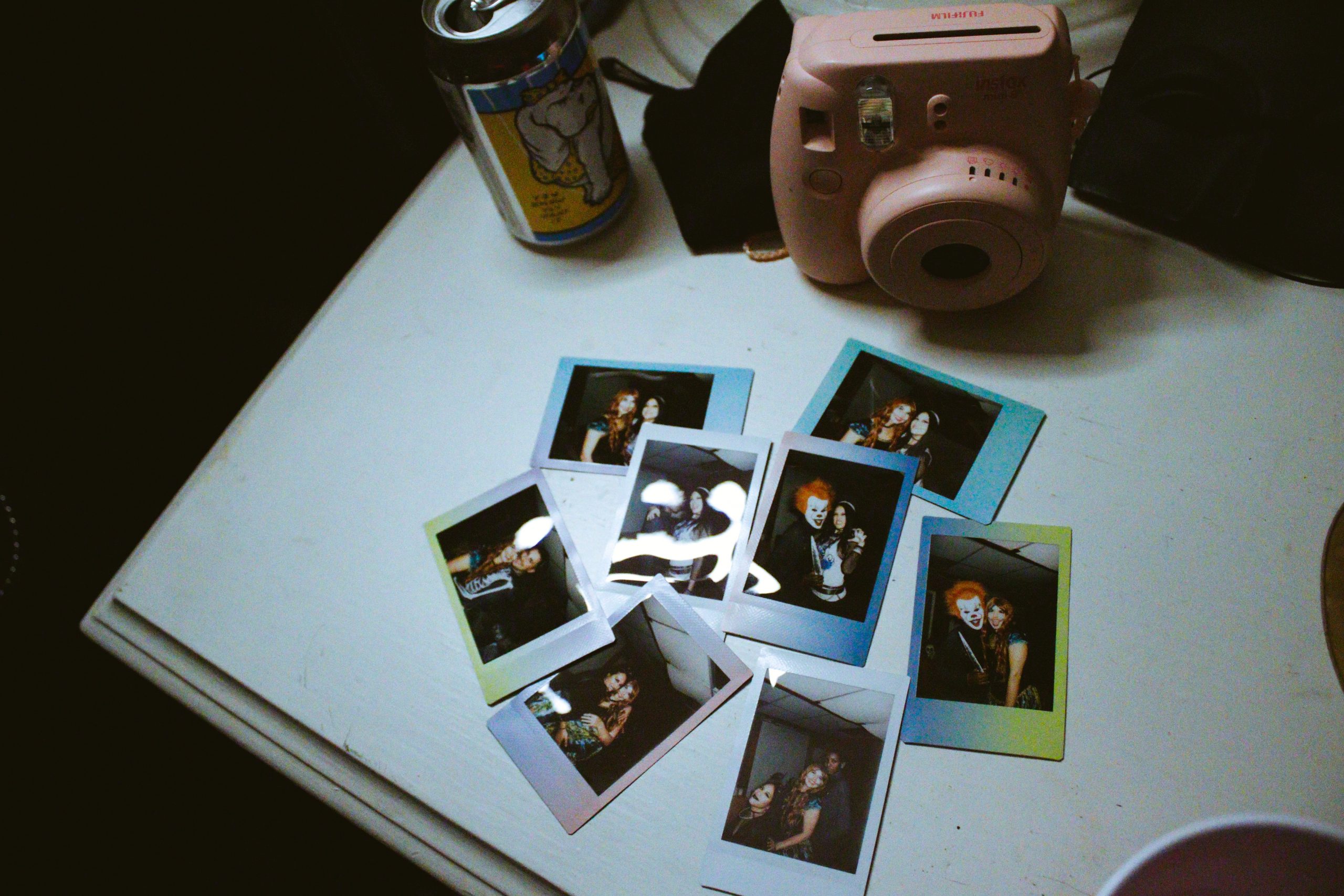 Polaroid camera, photos, and beverage can A pink polaroid camera, a beverage can, and photos on a table.