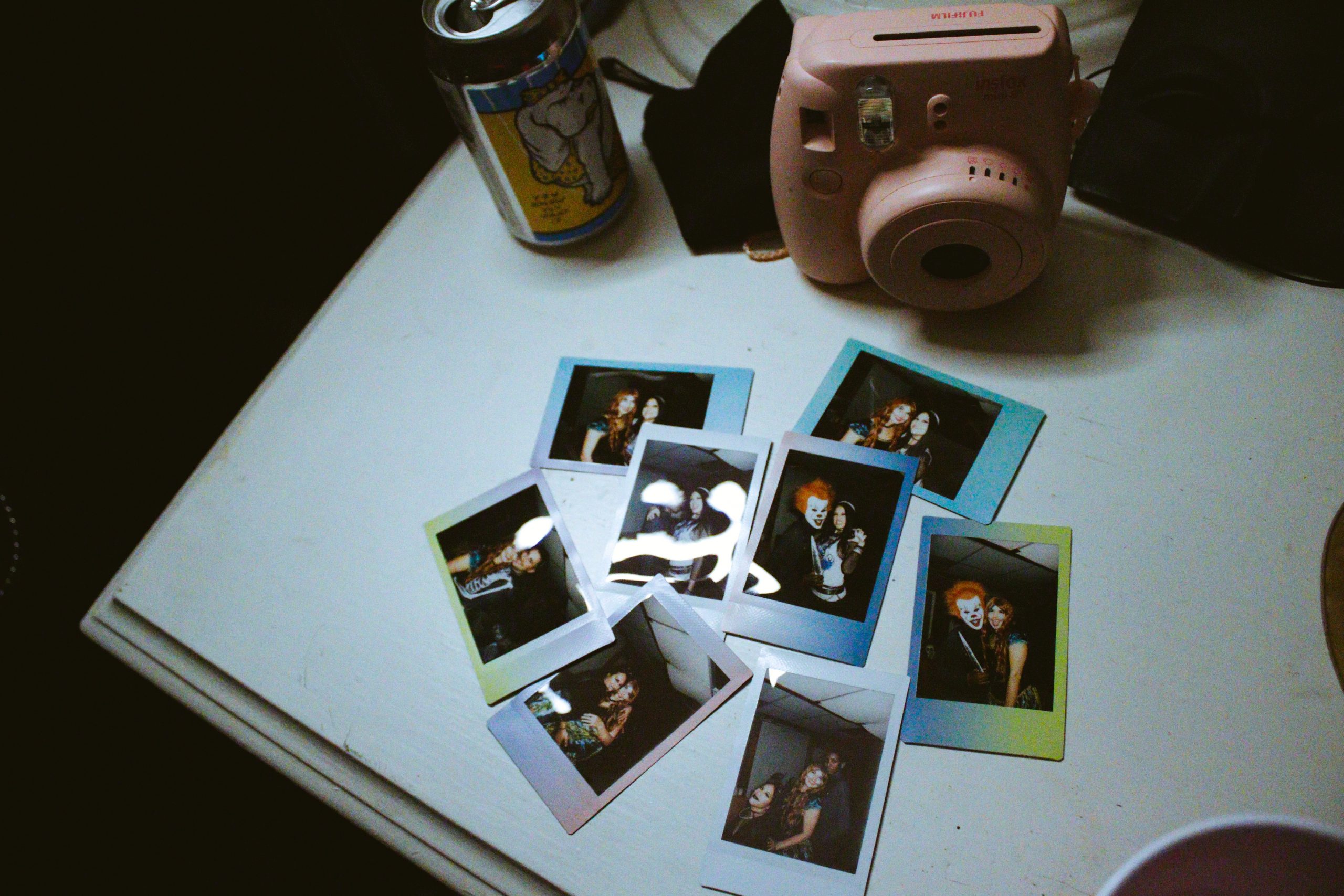 A pink polaroid camera, a beverage can, and photos on a table.