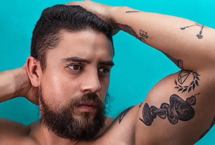 A bearded young man shows the wrapped around arm snake tattoo inked on his left bicep