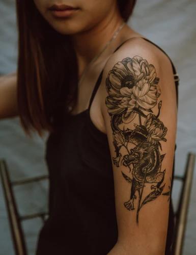 A lady showing her rose and snake tattoo on her left arm.