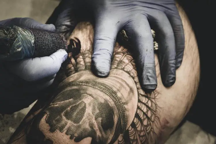 A snake with a skull tattoo being inked on a man’s left arm