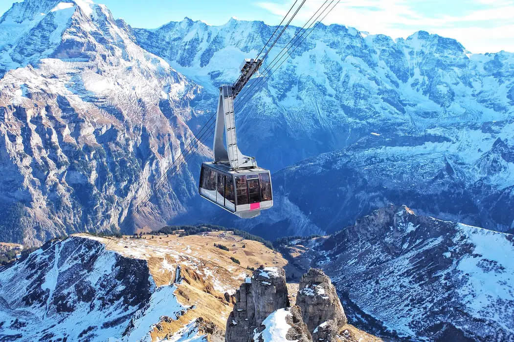 Image of a cable car moving through the high rises of Switzerland, surrounded by stunning beauty of mountains covered in snow.